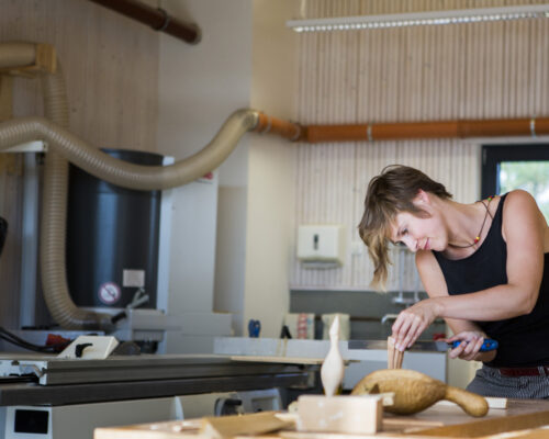 In der Holzwerkstatt ist eine Studentin, die an einem Stück Holz arbeitet.