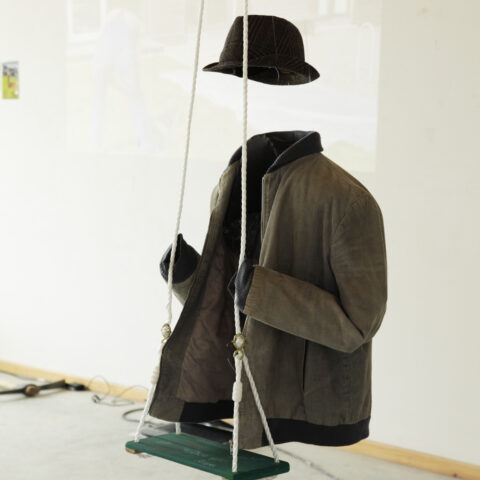 Titelbild für Stellenausschreibung - Kunstwerk einer unsichtbaren Person auf einer Schaukel (leerer Mantel und schwebender Hut)