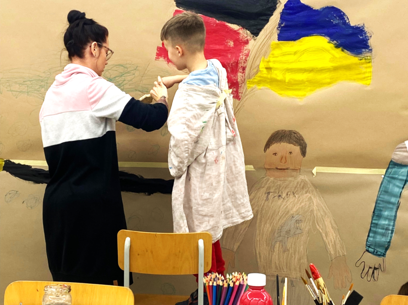 Das Bild zeigt eine Kunsttherapeutin beim Malen mit einem Kind.