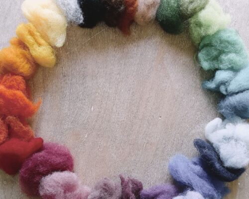 Farbenkranz aus bunter Filzwolle auf Holzuntergrund Kranzförmig auf einem hellen Holzhintergrund ausgelegte Büschel bunter Filzwolle, die einen weichen Farbverlauf von warmen Rot-, Orange- und Gelbtönen über Grün