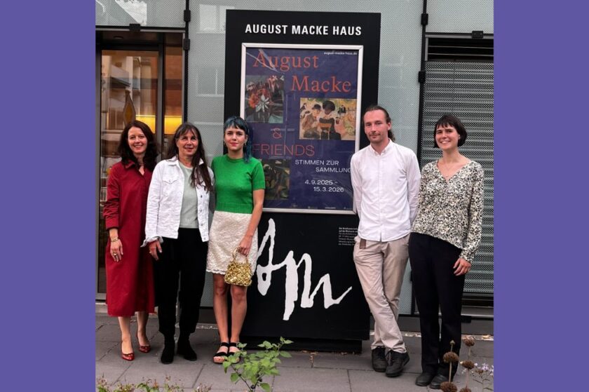 Fünf Personen stehen lächelnd vor dem Eingang des August Macke Haus, vor einem großen Plakat zur Ausstellung „August Macke & Friends – Stimmen zur Sammlung“. Di