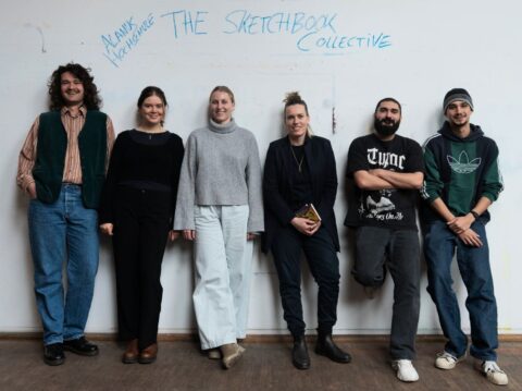 Sechs junge Erwachsene stehen lächelnd nebeneinander vor einer weißen Wand, auf der mit blauer Schrift „THE SKETCHBOOK COLLECTIVE“ und „Akane Hochschule“ geschr