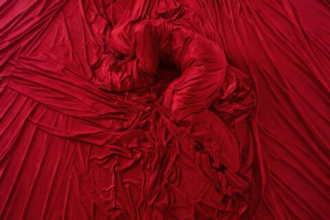 Nahaufnahme von reichlich drapiertem, knitterigem roten Stoff, der in der Mitte eine geschlungene, wurmförmige Struktur bildet.