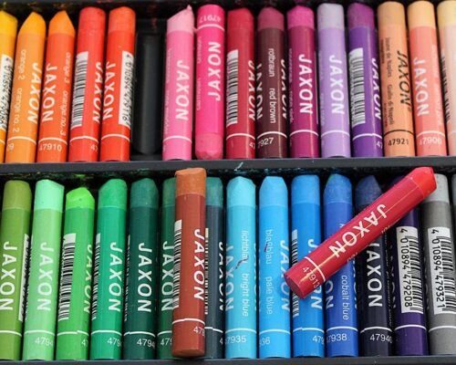 Bunte Wachspastellkreiden in einer Schachtel Nahaufnahme einer sortierten Schachtel mit vielen bunten Wachspastellkreiden der Marke Jaxon in zwei Reihen, von Gelb über Orange, Rot, Pink, Violett, Blau, Grü