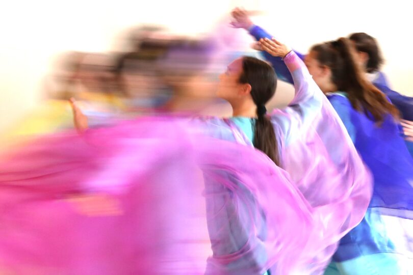 Eine Gruppe von Tänzerinnen in fließenden bunten Gewändern, die sich in einer verschwommenen Bewegung drehen.