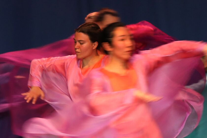 Verschwommene Aufnahme von Tänzerinnen in beweglichen, pinkfarbenen Gewändern während einer Tanzvorführung.