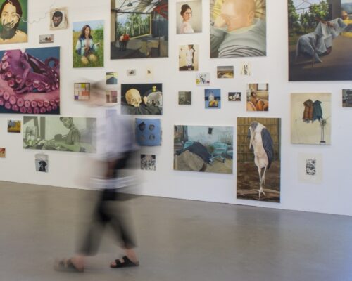 Galeriewand mit vielen unterschiedlich großen Gemälden und Illustrationen, unter anderem Porträts, Tierdarstellungen, Stillleben und abstrakte Motive; im Vorder