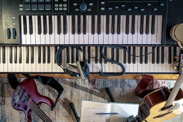 Draufsicht auf einen Musikarbeitsplatz mit zwei übereinander stehenden Keyboards, dazwischen ein aufgerolltes Kopfhörerkabel und Kopfhörer. Unten im Bild liegen