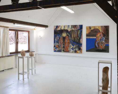 Heller Galerieraum mit weißem Boden und sichtbaren dunklen Holzbalken an der Decke. An der rechten Wand hängen zwei große, farbintensive Gemälde: links eine Sze