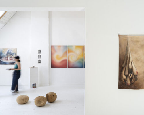 Helle Galerie mit weißen Wänden und abstrakten Gemälden: links betrachten zwei verschwommen vorbeigehende Personen die ausgestellten Werke, am Boden liegen drei