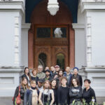 Zwischen Seidenstraße und Gegenwartskunst 2 Gruppenfoto von etwa zwanzig Menschen unterschiedlichen Alters vor einem großen, dekorativen Holztor eines historischen Gebäudes. Die Gruppe steht eng beisammen