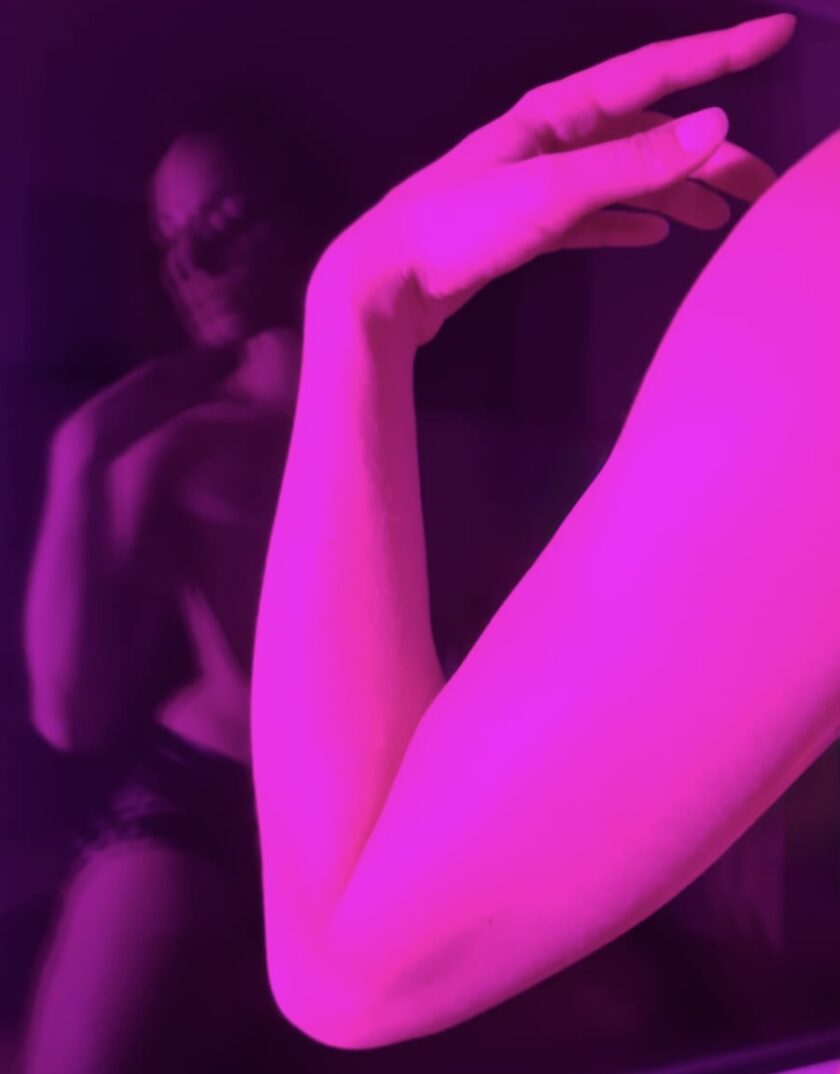 Abstrakte Aufnahme eines ausgestreckten Arms und einer Hand in intensivem pink-violetten Licht, im Hintergrund schemenhaft ein Oberkörper.