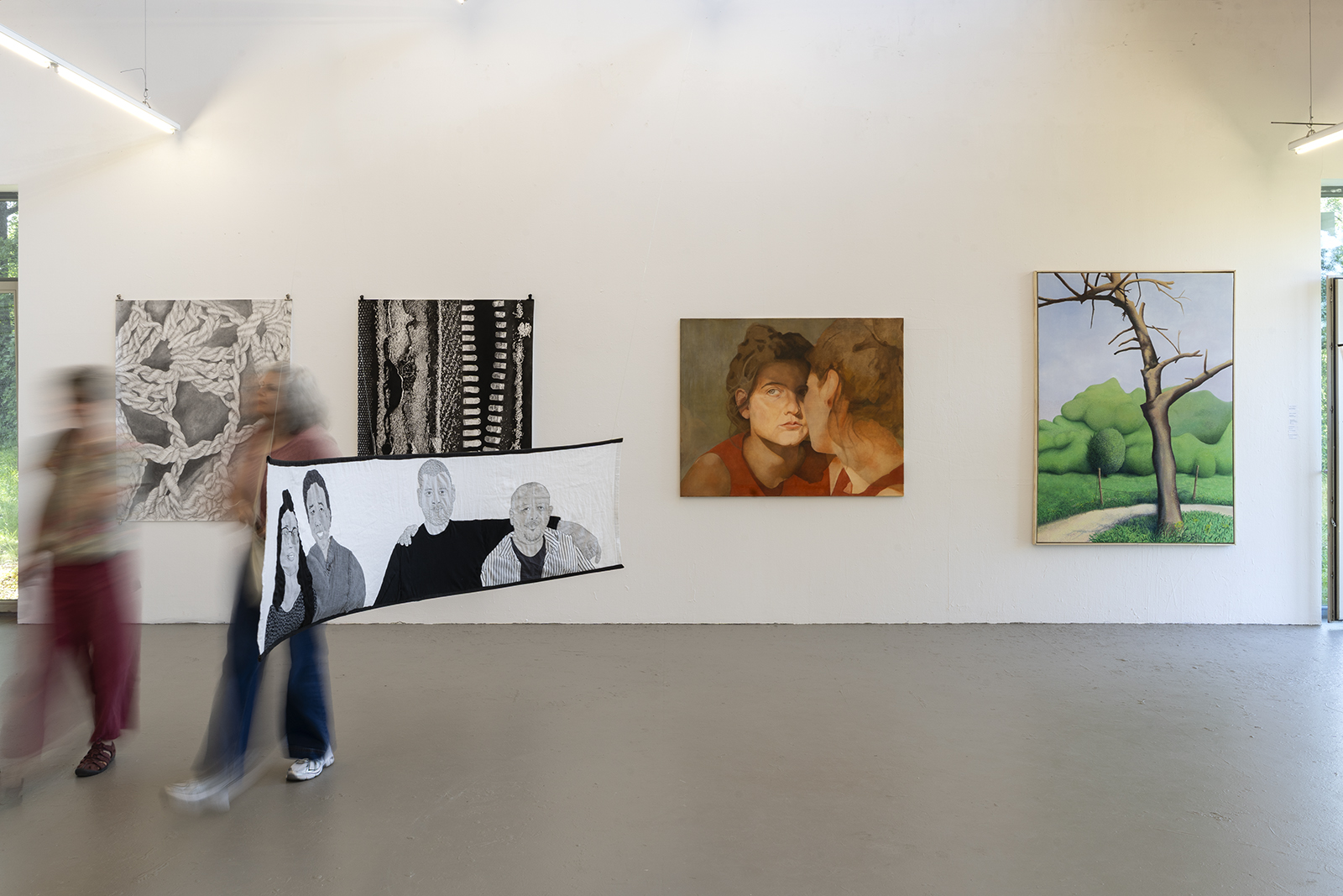Innenansicht eines hellen Ausstellungsraums mit vier an einer weißen Wand hängenden Kunstwerken: links eine graue, abstrakte Strukturzeichnung, daneben ein hoch