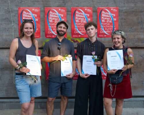 von Links: Emilie Fank, Niklas van Megen, Leon Steinbauer, Lia Gönner Vier junge Erwachsene stehen nebeneinander vor einer Holzwand mit roten Plakaten der Alanus Hochschule. Alle halten eine Urkunde und eine einzelne Blume in den