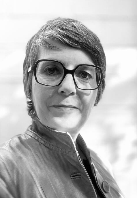 Schwarz-weiß-Porträt einer Person mit kurzem, seitlich frisiertem Haar und großer eckiger Brille, die mit ernstem, ruhigem Gesichtsausdruck in die Kamera schaut